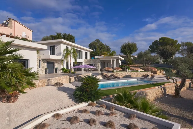 Jardin minéral planté de graminées et de palmiers devant la piscine et la villa
