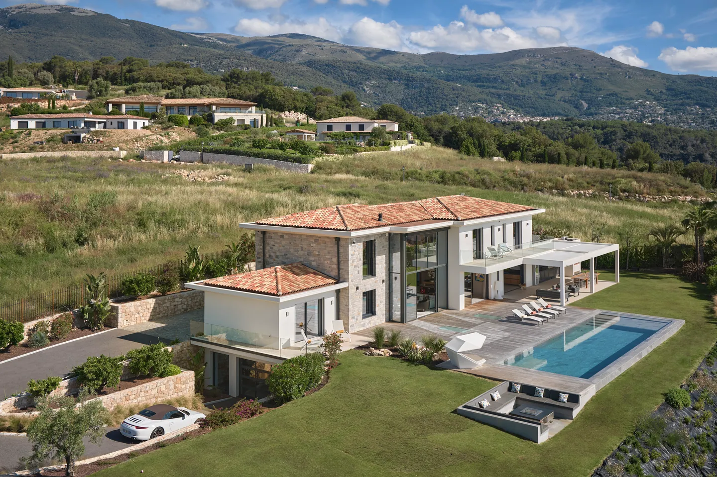 Villa en pierre et enduit blanc sous tuiles, piscine et salon extérieur sur pelouse