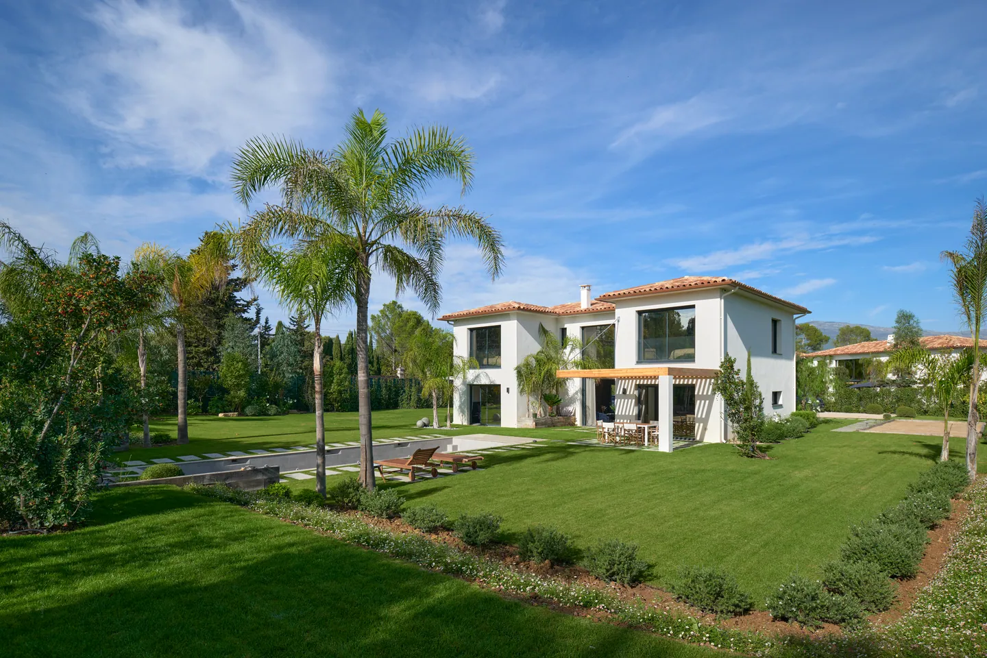 Villa blanche à toits de tuiles vue depuis la pelouse, palmiers et pergola en bois
